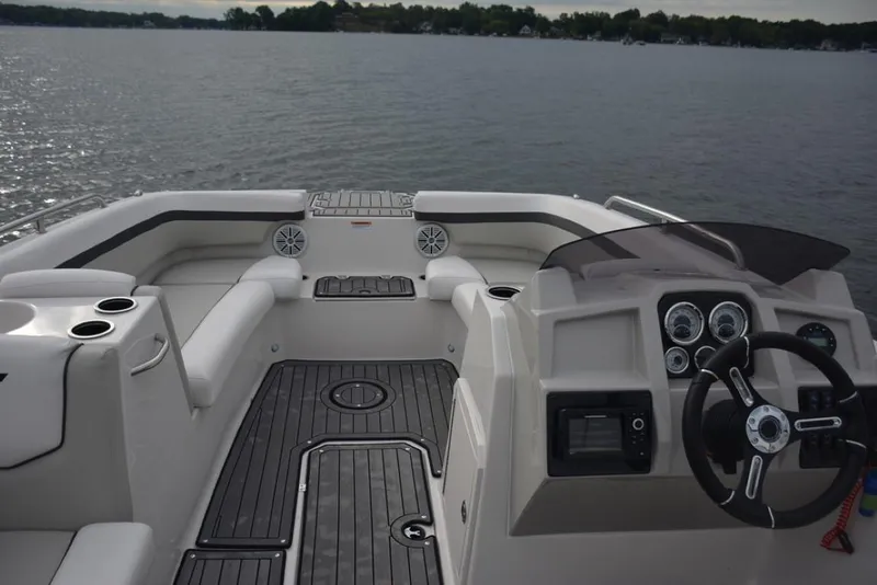 Slide: The Image of 2023 Starcraft 211 SVX boat interior with steering wheel and seating, on a calm lake. - 14