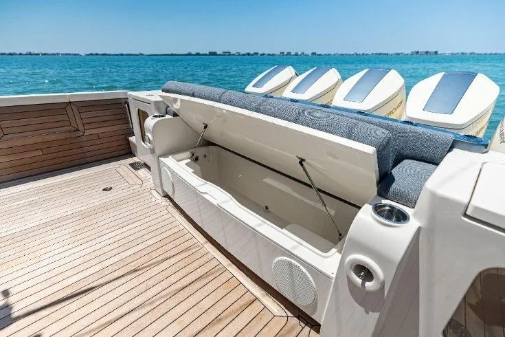 Slide: The Image of 2026 Scout 670 LXS boat with open storage compartment, wooden deck, and ocean backdrop. - 17