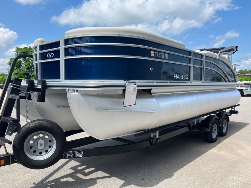 The Image of 2023 Harris Cruiser 230 pontoon boat on trailer under a blue sky. - 0