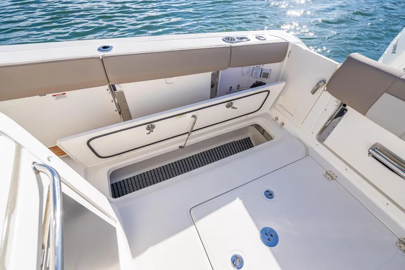 Slide: The Image of 2026 Boston Whaler 420 Outrage boat deck with open storage compartment, near water. - 54
