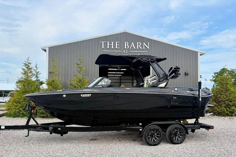 The Image of 2025 Centurion NV 213 boat on trailer, parked outside a barn, surrounded by trees. - 1