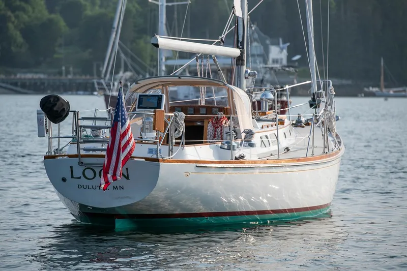 Slide: The Image of 1988 Hinckley Sou'wester 42 sailboat on water, displaying American flag, docked near shoreline. - 6