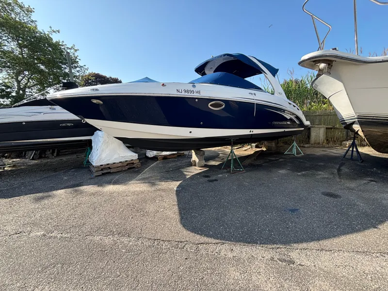 Slide: The Image of 2012 Chaparral 287 SSX boat on stands, blue and white hull, parked outdoors. - 0
