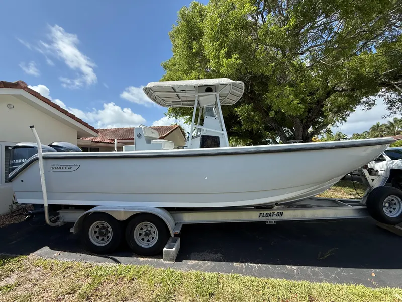 The Image of 2005 Boston Whaler 260 Outrage boat on trailer, parked outdoors under a tree. - 0