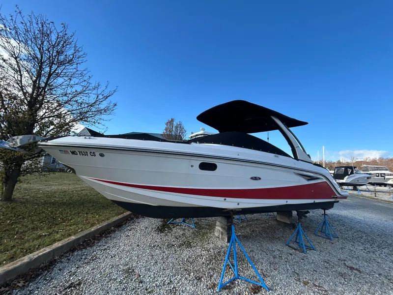 The Image of 2018 Sea Ray SLX 280 boat on stands, white with red stripe, clear blue sky. - 1