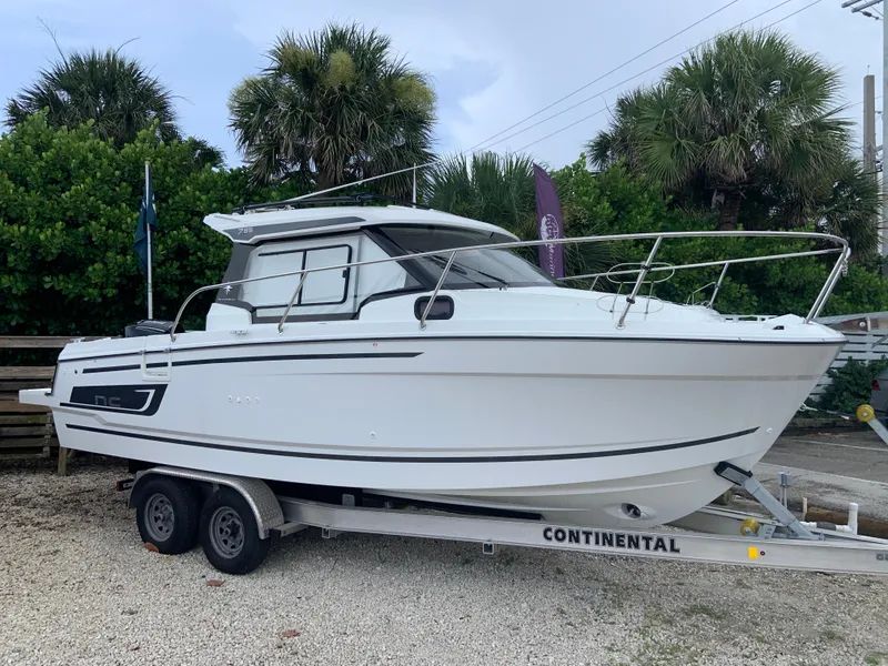 The Image of 2023 Jeanneau NC795 S2 boat on trailer, surrounded by palm trees. - 0