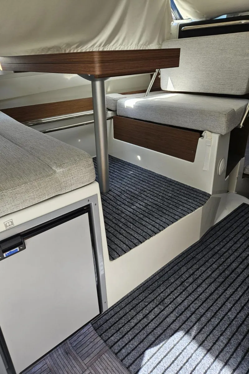 Slide: The Image of 2023 Jeanneau NC795 S2 interior with seating, table, and compact fridge. - 19