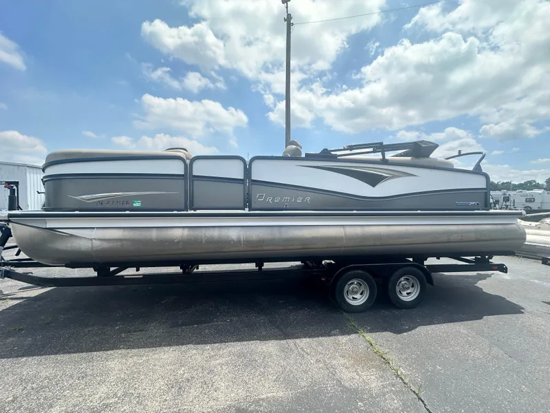 The Image of 2023 Premier 250 Solaris pontoon boat on a trailer under a partly cloudy sky. - 1