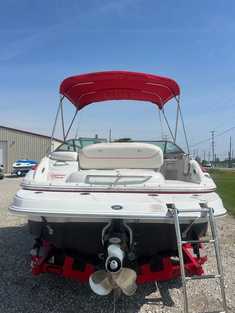 Slide: The Image of 2007 Crownline 220 EX boat with red canopy and ladder, parked on gravel. - 2