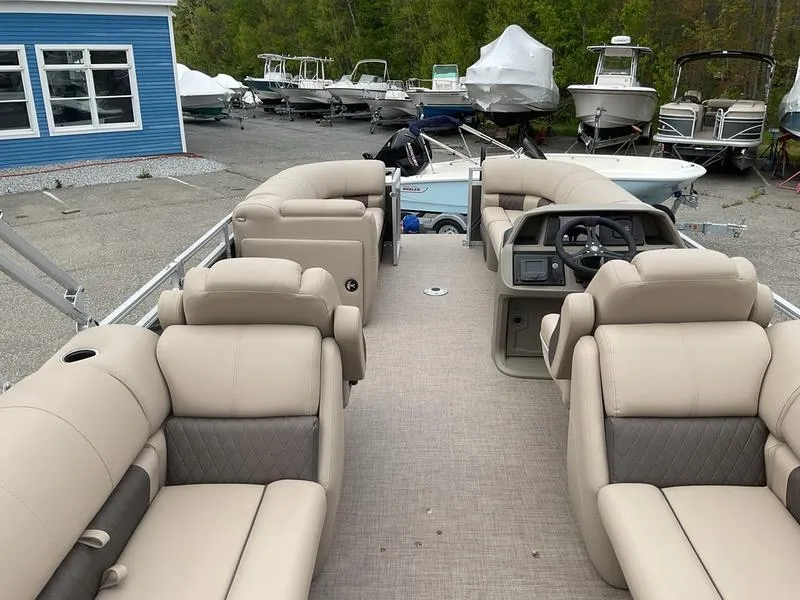Slide: The Image of 2025 Sun Tracker PARTY BARGE® 22 DLX interior with beige seating, parked among other boats. - 6