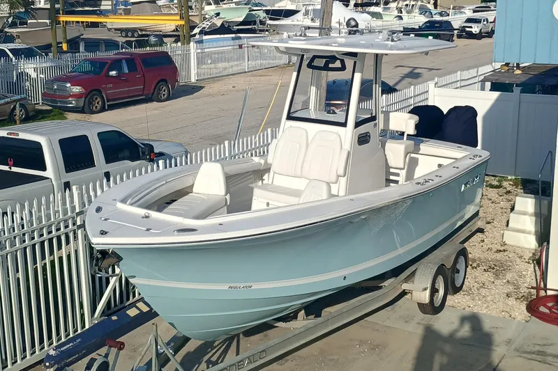 Slide: The Image of 2025 Regulator 23 boat on trailer, parked in marina lot with surrounding vehicles. - 2