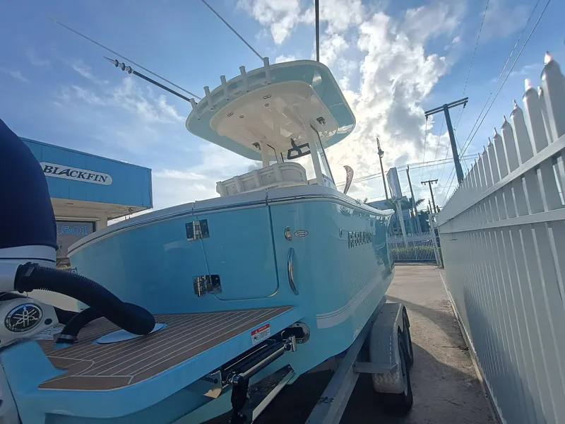 Slide: The Image of 2025 Regulator 23 boat on trailer, blue hull, parked near fence under cloudy sky. - 4