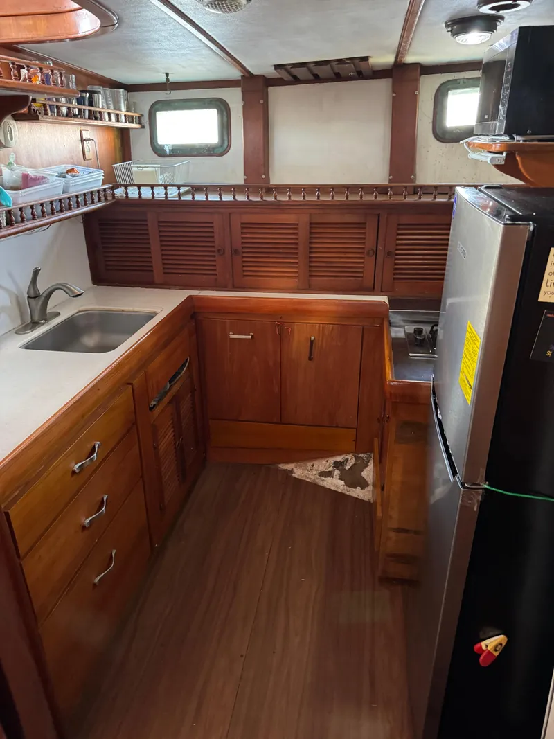Slide: The Image of 1983 Island Trader Motor Sailor kitchen with wooden cabinets, stainless steel sink, and compact appliances. - 13
