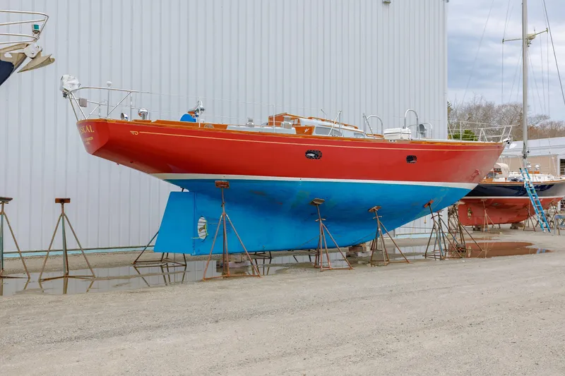Slide: The Image of 1972 Hinckley 48 sailboat on stands, red hull, blue bottom, docked outdoors. - 2
