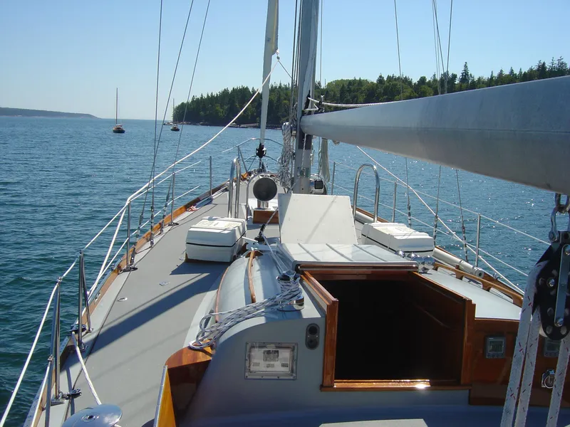 Slide: The Image of Hinckley 48 sailboat deck view, 1972 model, sailing on calm waters near a forested shoreline. - 25