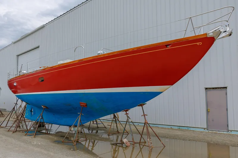 Slide: The Image of 1972 Hinckley 48 sailboat with red and blue hull on stands, near a warehouse. - 7