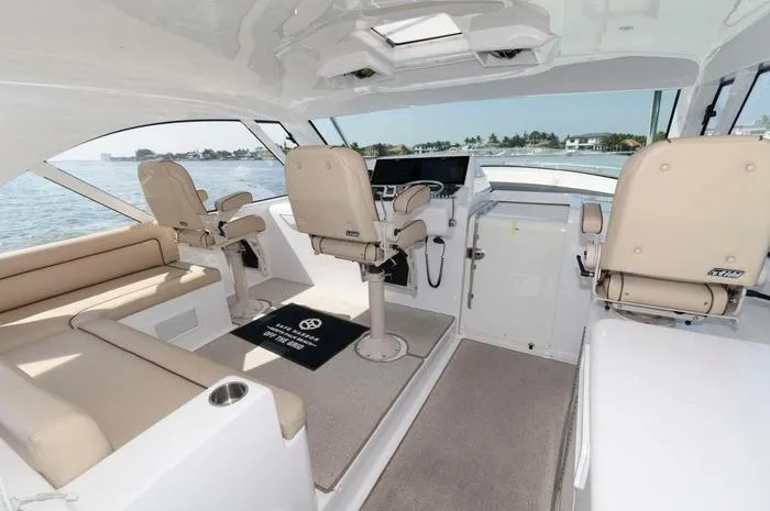 Slide: The Image of 2015 Hatteras 45 Express Sportfish interior with beige seating and helm, overlooking water. - 18