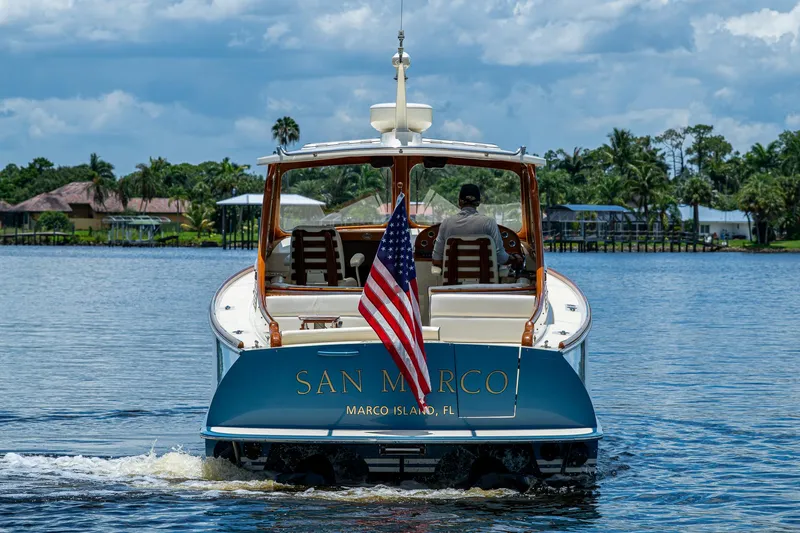 Slide: The Image of Hinckley Talaria 34 boat cruising on water, American flag, lush tropical background. - 2