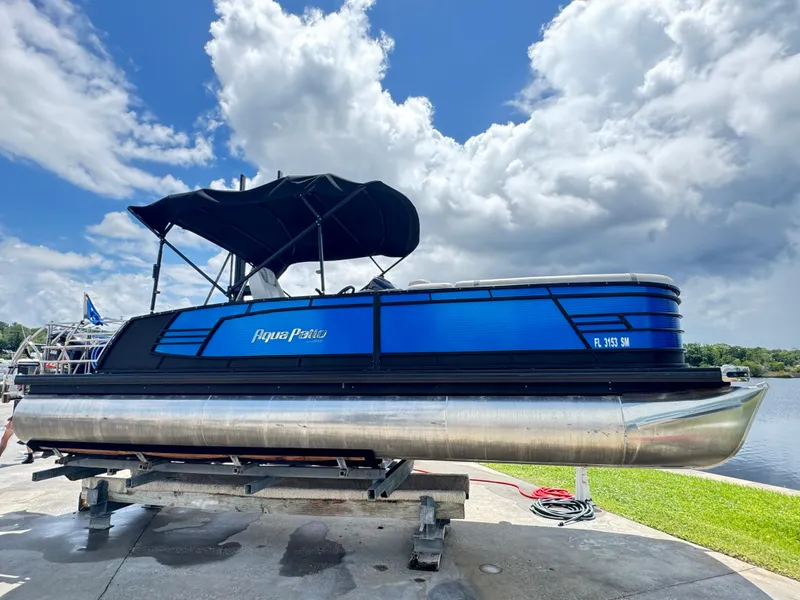 Slide: The Image of 2019 AquaPatio 259 DFL pontoon boat on a lift, under a partly cloudy sky. - 0