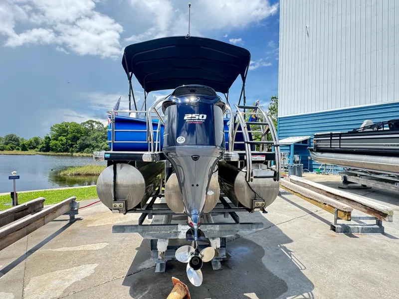 Slide: The Image of 2019 AquaPatio 259 DFL pontoon boat on trailer near a lake and building. - 1