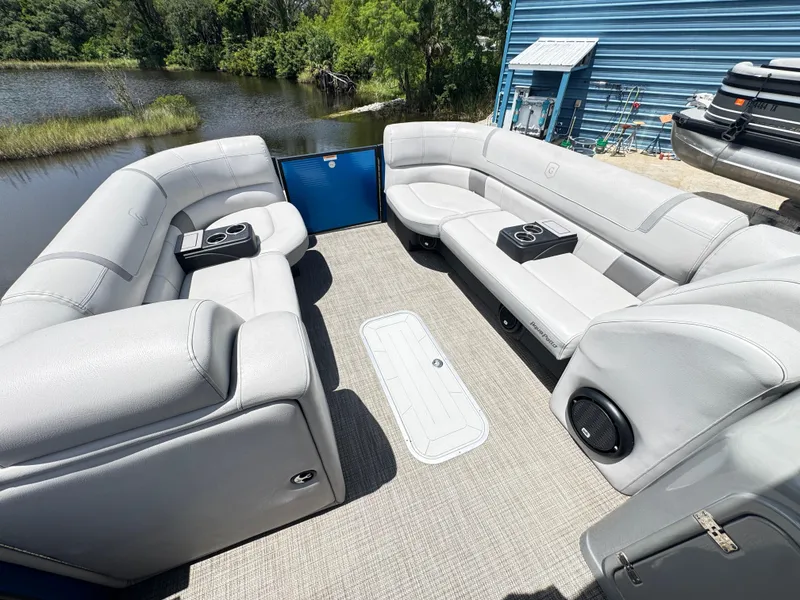 Slide: The Image of 2019 AquaPatio 259 DFL pontoon boat interior with gray seating and cup holders by a lake. - 2