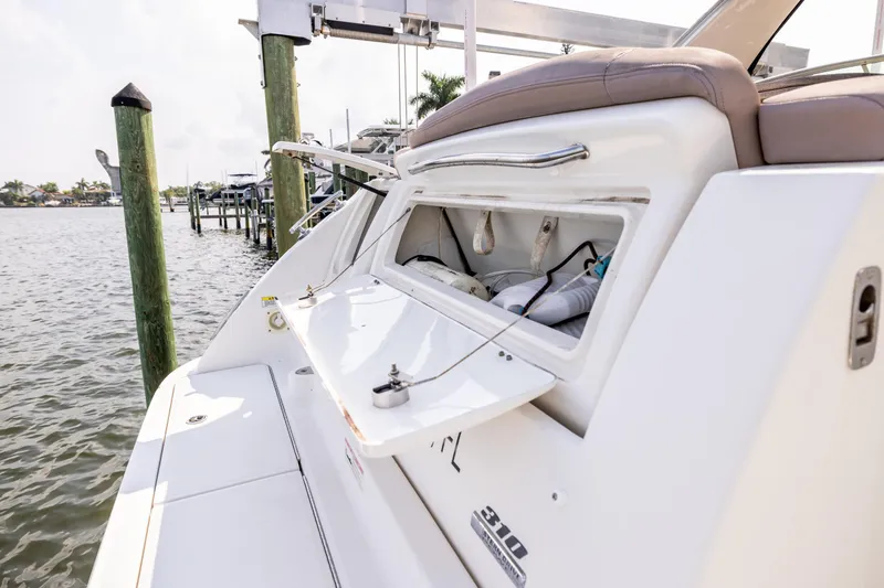 Slide: The Image of 2016 Sea Ray 310 Sundancer boat with open storage compartment, docked by the water. - 22