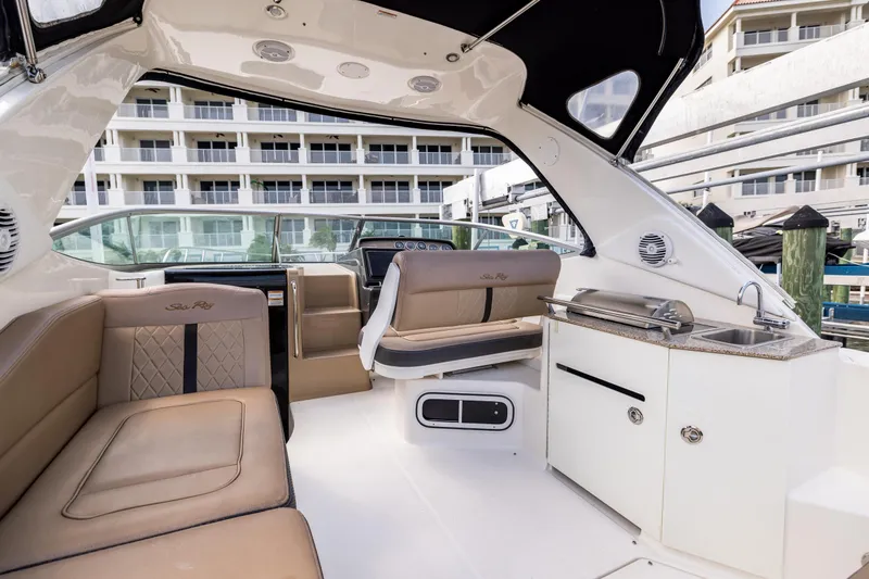 Slide: The Image of 2016 Sea Ray 310 Sundancer interior with seating, kitchenette, and helm, docked near buildings. - 28