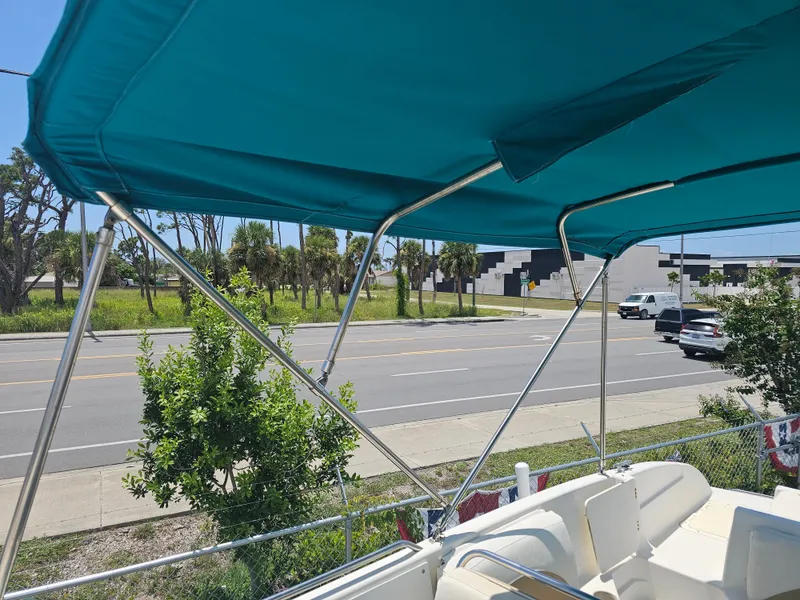 Slide: The Image of 1996 Bayliner 2609 Rendezvous boat with teal canopy, parked near a road. - 26