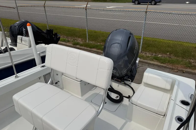 Slide: The Image of 2025 Parker 181 SHOAL boat with white seating and outboard motor, parked near a fence. - 8