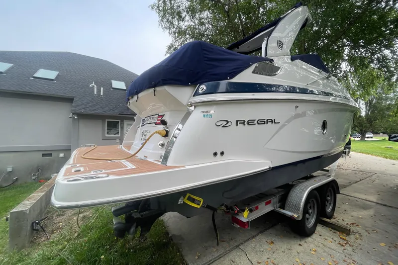 Slide: The Image of 2019 Regal 28 Express boat on trailer, parked near a house with trees in the background. - 2