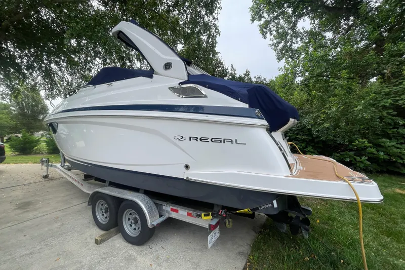 Slide: The Image of 2019 Regal 28 Express boat on trailer, parked outdoors with trees in the background. - 46