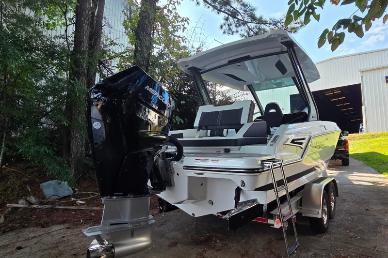 Slide: The Image of 2026 Monterey Elite 27 OB boat with Mercury outboard engine, parked near trees and a building. - 13
