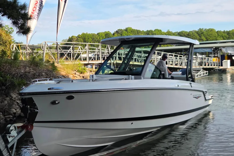 Slide: The Image of 2026 Monterey Elite 27 OB boat docked near a marina with lush greenery. - 14