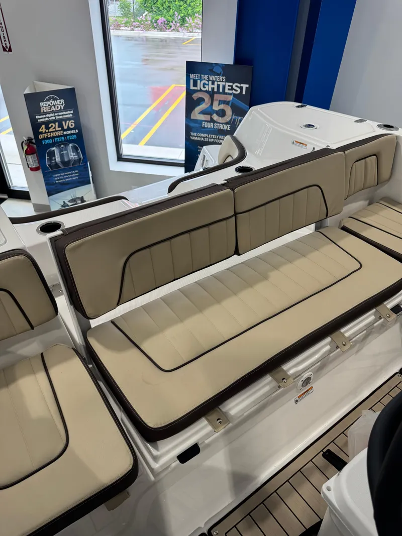 Slide: The Image of 2025 Yamaha Boats 255 FSH Sport E interior seating with beige cushions in showroom. - 22