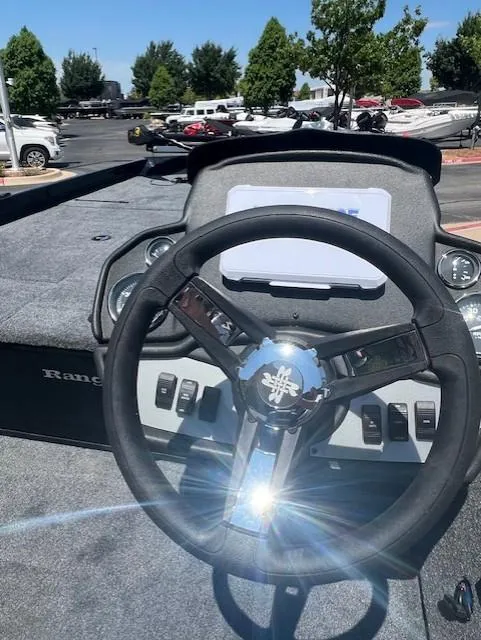 Slide: The Image of Steering wheel of 2025 Ranger RT188 boat, parked outdoors with trees in background. - 7