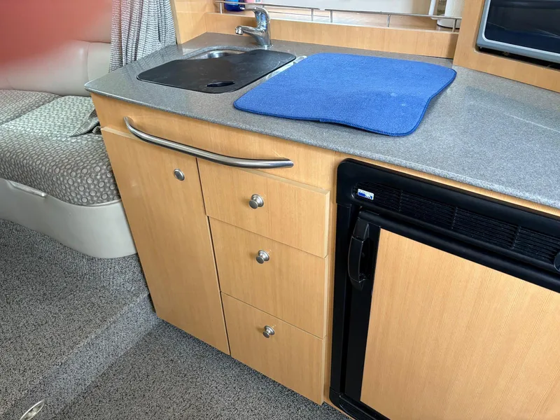Slide: The Image of 2004 Maxum 3100 SE boat interior with kitchenette, featuring sink, drawers, and mini fridge. - 16