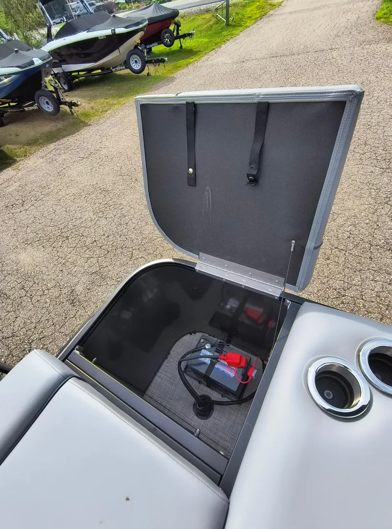 Slide: The Image of Open storage compartment in 2025 SunCatcher Fusion 322C boat, showing battery and cup holders. - 28