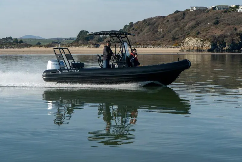 Slide: The Image of 2024 Highfield Patrol 600 boat cruising on calm water near rocky shoreline. - 3