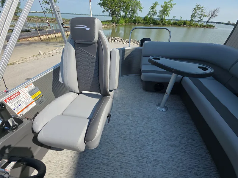 Slide: The Image of 2025 Bennington 20 SL boat interior with gray seating and table, near a scenic lake. - 9