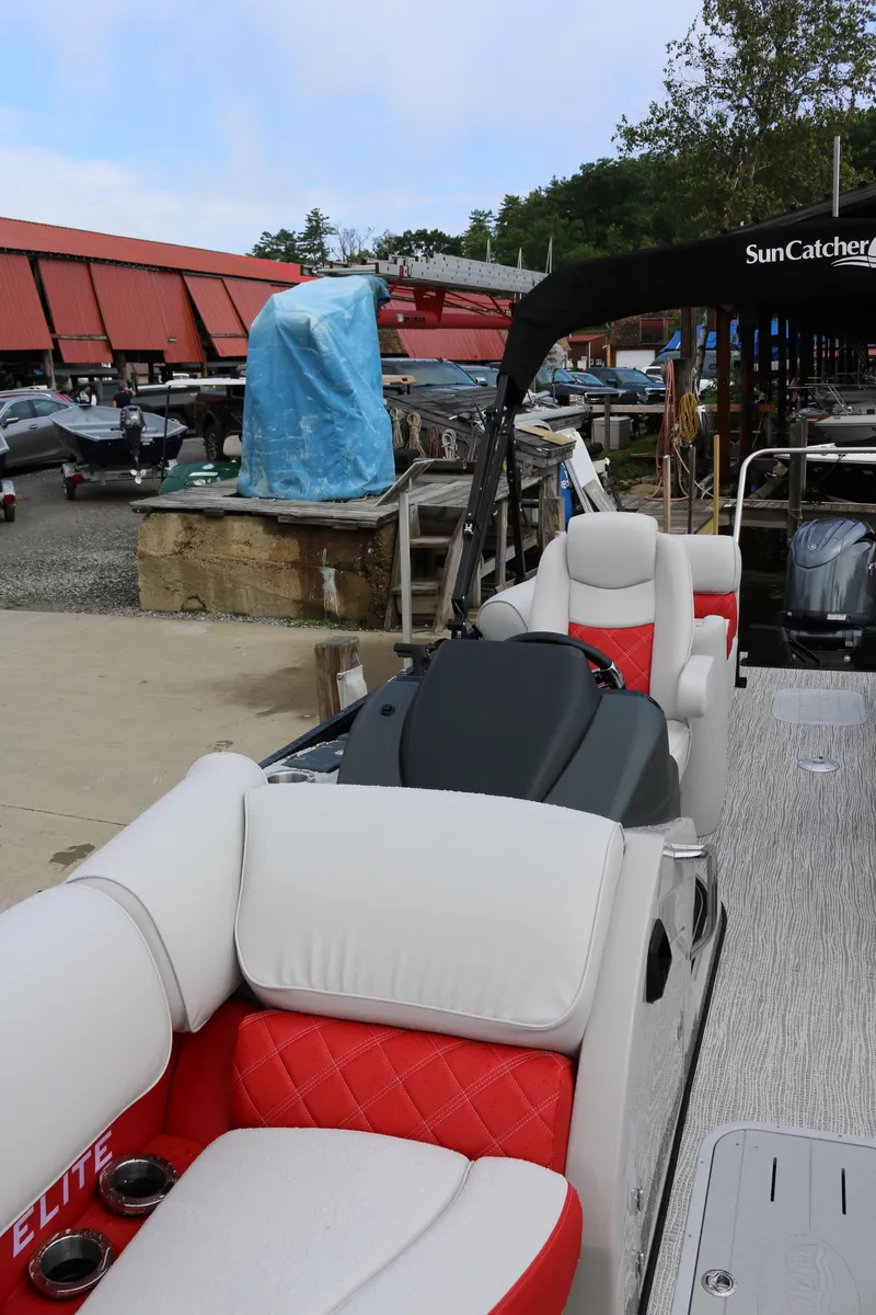 Slide: The Image of 2025 SunCatcher Elite 324 RC pontoon boat with red and white seating at a marina. - 6
