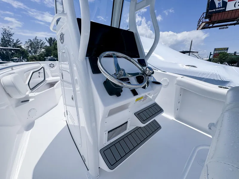 Slide: The Image of 2026 Tidewater 232 CC Adventure boat helm with steering wheel and console, under clear blue sky. - 9