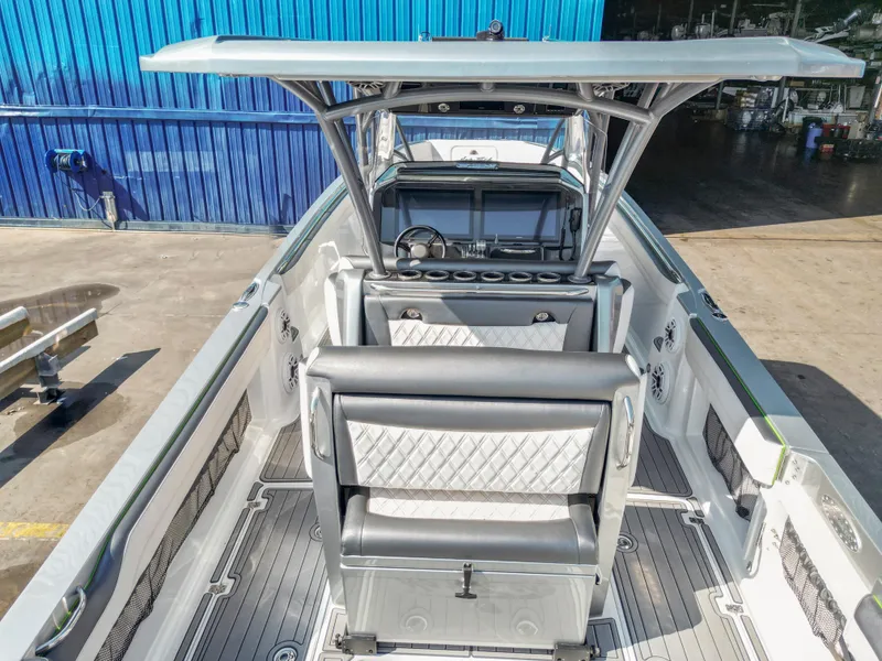 Slide: The Image of 2021 Nor-Tech 390 Sport Center Console boat interior with seating and helm, docked near blue building. - 20