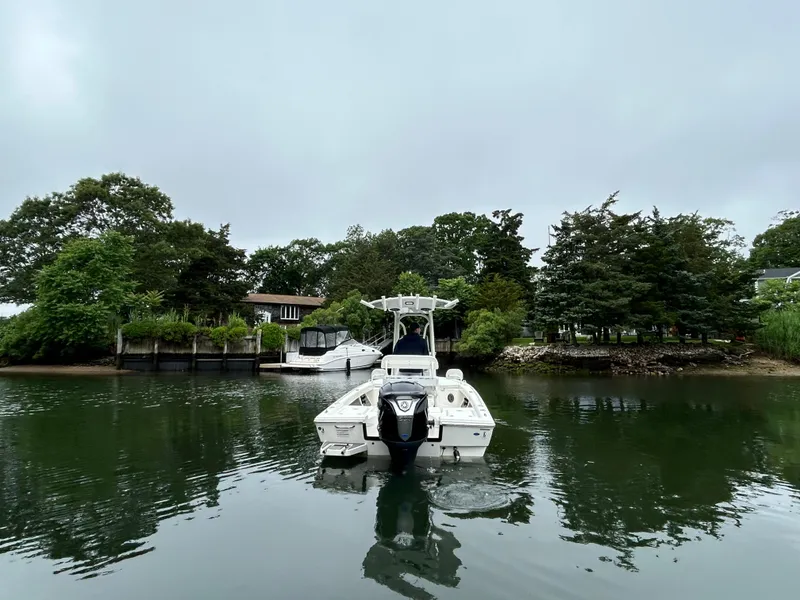 Slide: The Image of 2024 Pathfinder 2200 TRS boat on calm water near lush greenery and docked vessels. - 2