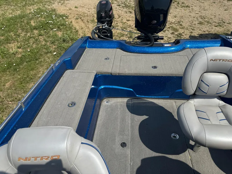 Slide: The Image of 2018 Nitro ZV21 boat interior with gray seats and blue accents, parked on grass. - 11