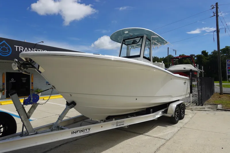 Slide: The Image of 2026 Sea Hunt Gamefish 25 boat on trailer, parked outside dealership under clear blue sky. - 2