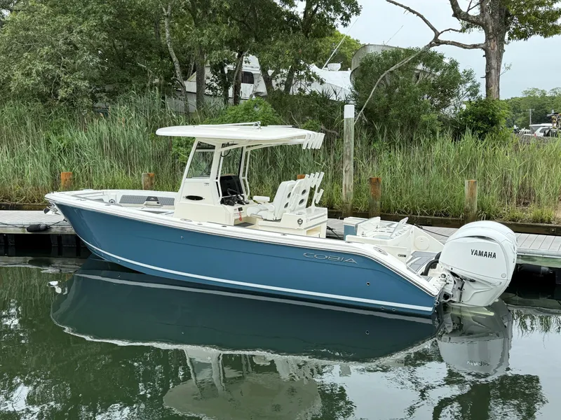 Slide: The Image of 2025 Cobia 265 Open Center Console boat docked, featuring Yamaha engine, surrounded by lush greenery. - 2