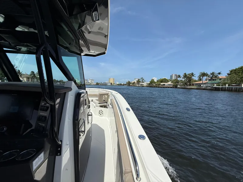 Slide: The Image of 2020 Blackfin 332 CC boat cruising on a sunny waterway with cityscape views. - 13