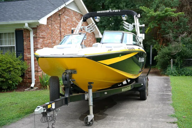 Slide: The Image of 2014 MasterCraft X-25 boat on trailer in front of brick house, surrounded by trees. - 1