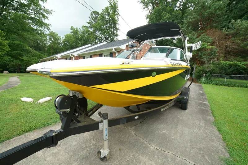 Slide: The Image of 2014 MasterCraft X-25 boat with yellow and black design on a trailer in a driveway. - 48
