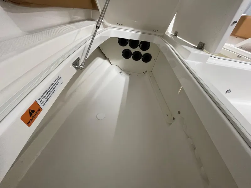 Slide: The Image of 2025 Robalo 246 Cayman storage compartment with warning label and hydraulic support. - 10